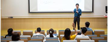 teacher in blue shirt answers question from a female student in yellow t-shirt
