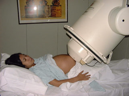 A pregnant woman lying on her back in a bed, with her belly exposed and a white machine positioned just over her belly.