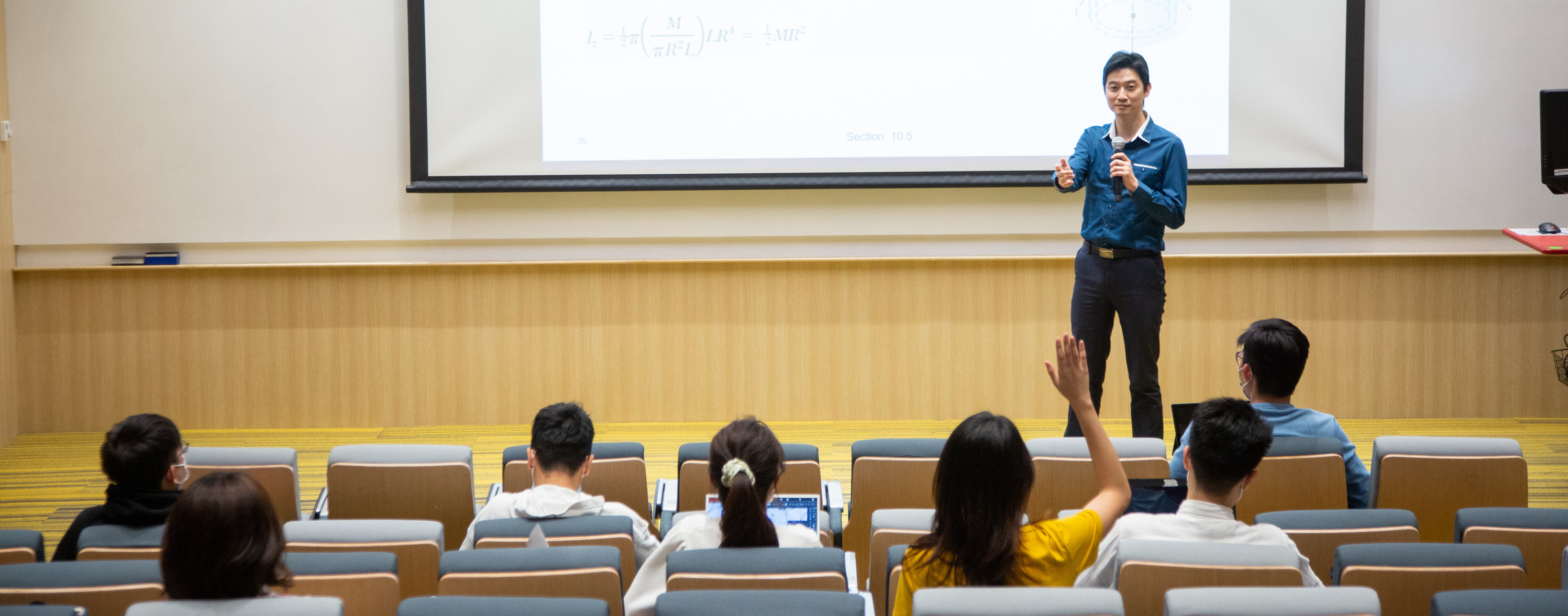teacher in blue shirt answers question from a female student in yellow t-shirt