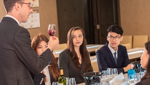 Students in suit sit around the table and have wine tasting class